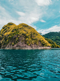 Scenic view of sea by mountain against sky