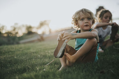 Siblings wearing shoes while sitting on grassy field in backyard