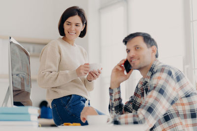 Smiling woman looking at computer while man talking on phone