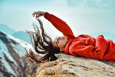 Woman tossing hair while lying on rock against sky