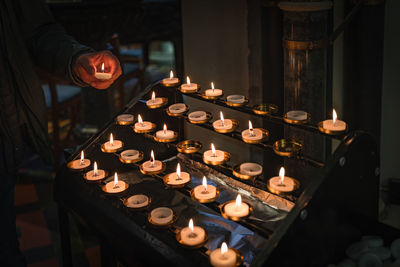 Cropped hand of person holding illuminated candles on table