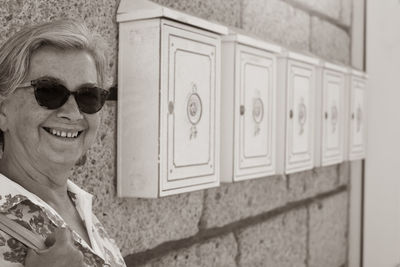 Portrait of happy woman wearing sunglasses against cabinets on wall