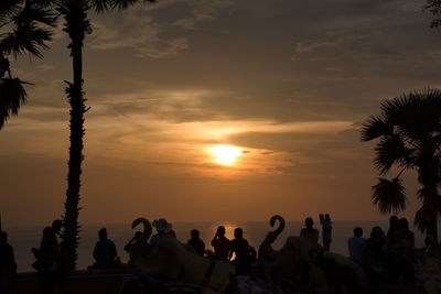 Silhouette people on palm tree against sky during sunset