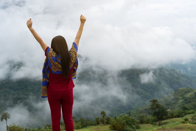 Rear view of woman with arms raised against sky