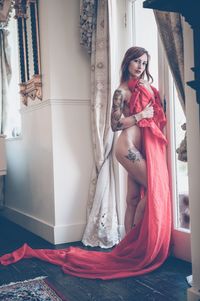 Portrait of naked woman holding red textile at home
