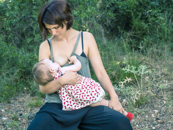 Mother breastfeeding toddler daughter while kneeling at park