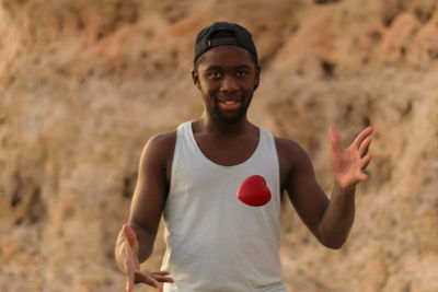 Portrait of young man catching red heart shape against rock formation