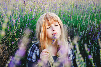 Beautiful young woman holding lavender flowers while sitting in lavender field