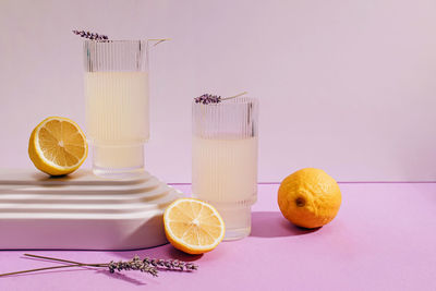 Still life composition with lavender lemonade and lemons on purple background, harsh shadows