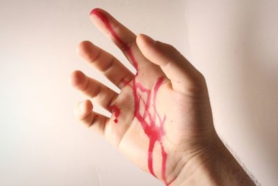 Cropped hand of man with blood against wall