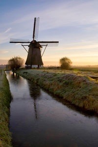 Traditional windmill on field against sky during sunset