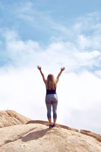 Rear view of woman standing on rock against sky