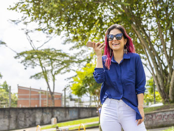 Portrait of smiling young woman wearing sunglasses against trees