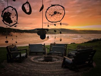 Deck chairs at beach against sky during sunset