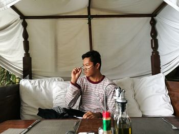 Young man looking away while sitting on sofa in yard