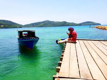 Woman sitting on pier over lake against sky