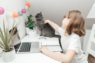 Distance learning at home.the girl studies online at home, sits at a laptop and strokes a gray cat. 