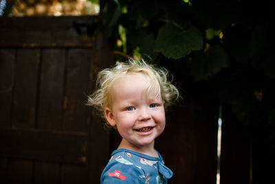 Blond two year old boy smiling for camera standing in yard