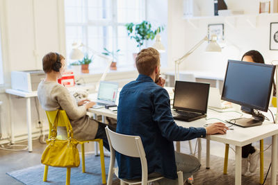 Multi-ethnic colleagues using laptops while working at desk in illuminated creative office