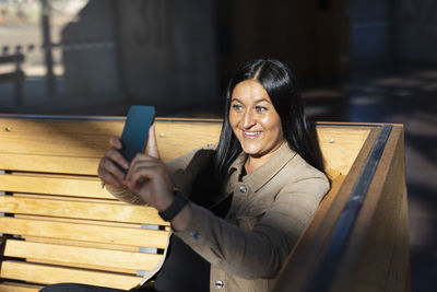 Smiling woman sitting on back at train station and taking selfie