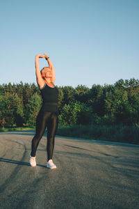 Full length of woman exercising while standing on road