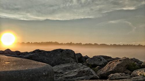 Rocks by sea against sky during sunset