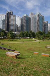 Park bench by buildings in city against sky