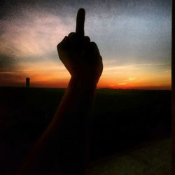 Silhouette hand against orange sky during sunset