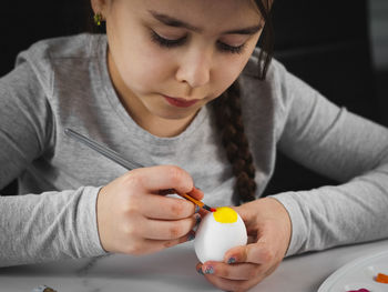 Little caucasian girl in a gray turtleneck enthusiastically paints an easter egg