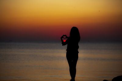 Silhouette man standing on beach against sky during sunset