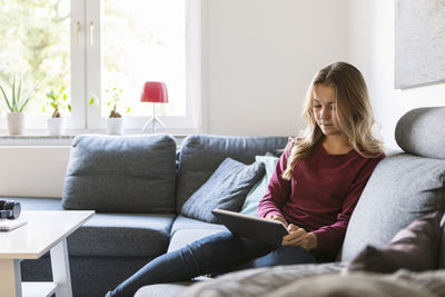 Female teenager using digital tablet while sitting on sofa at home