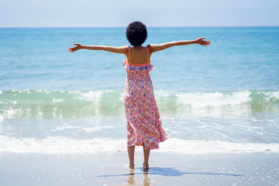 Rear view of woman with arms outstretched standing on beach