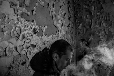 Side view of man standing against weathered wall