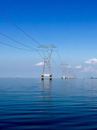 Electricity pylon by sea against blue sky