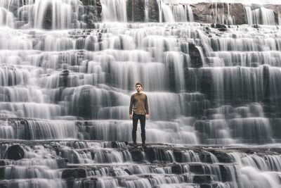 Portrait of young man standing against waterfall