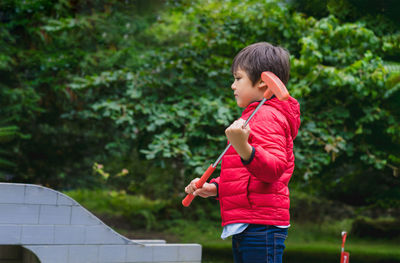 Side view of boy holding sports equipment against trees in park