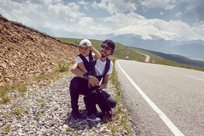 Father and son in caps and sunglasses catch a car standing on the road in the mountains