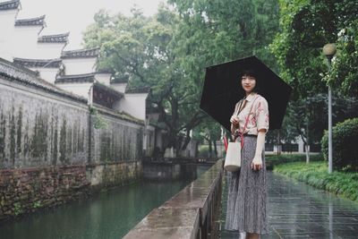 Woman with umbrella standing by plants during rainy season