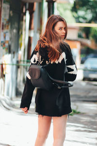 Portrait of beautiful woman with backpack walking on street in city