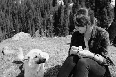 Woman holding food while sitting with dog on mountain