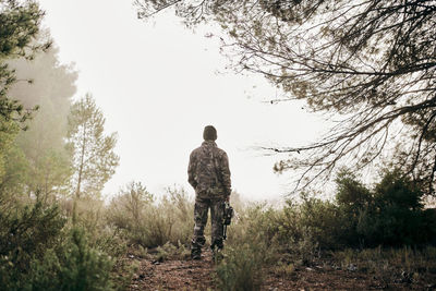 Rear view of man standing amidst trees against sky