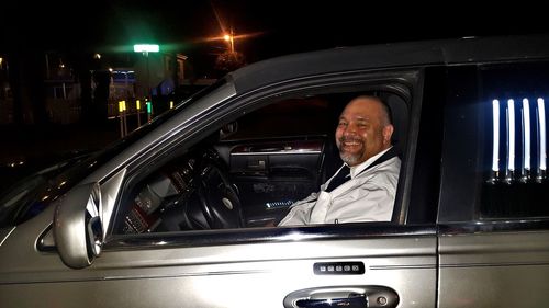 Portrait of smiling man standing on car at night