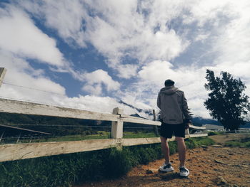 Rear view of man standing on landscape against cloudy sky