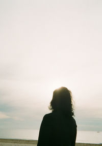 Rear view of silhouette woman standing by sea against sky