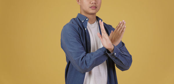 Young man looking away while standing against yellow background