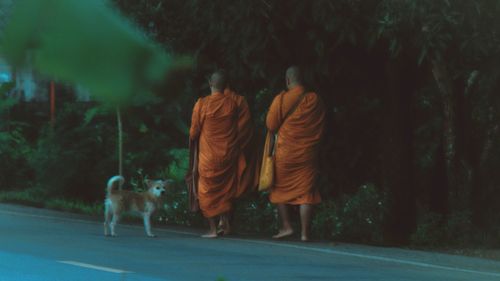 Rear view of monks walking on road by trees
