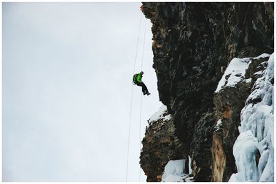 Man skiing on cliff against sky during winter