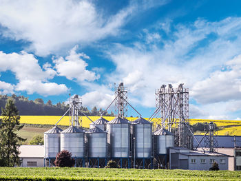 Grain silo plant against the field of ripening raps flowers