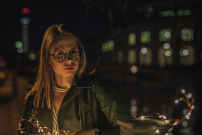 Close-up young woman holding illuminated string light at night