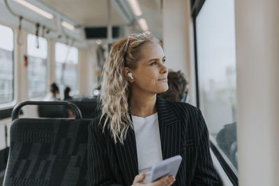 Blond businesswoman listening to music while sitting with smart phone in train